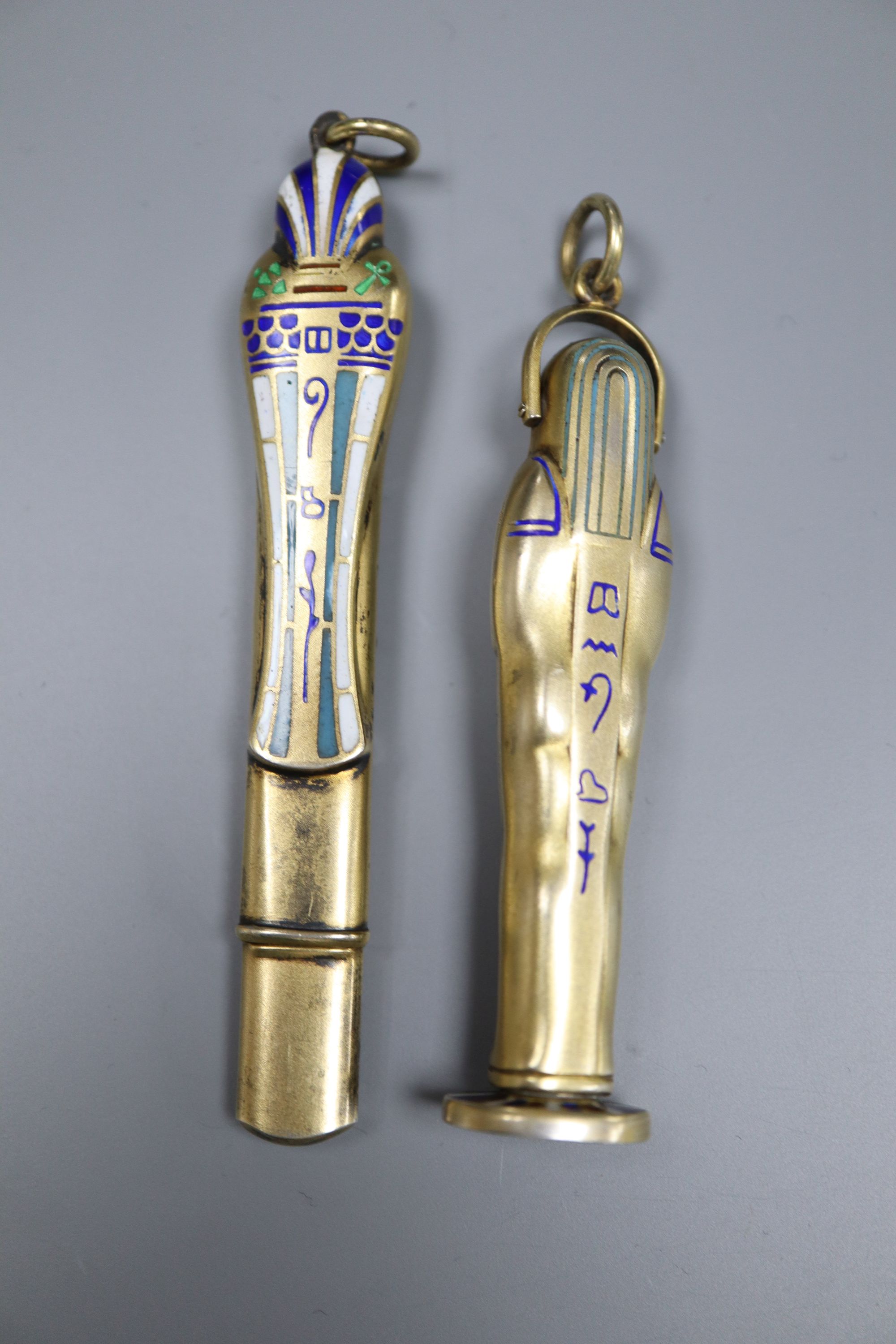 An early 20th century Egyptianesque gilt white metal and enamel propelling pencil/seal, 59mm and a similar pencil case, 72mm.